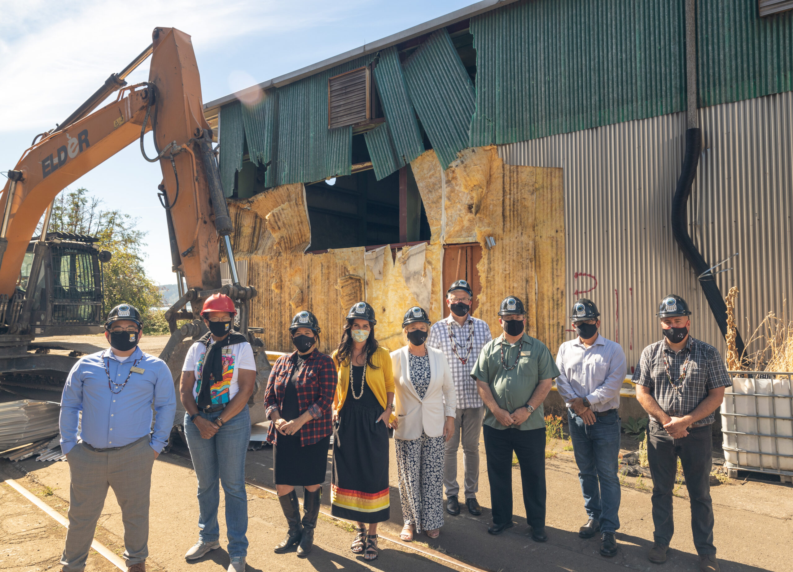 Public and Tribal officials in front of an old warehouse and construction equipment.